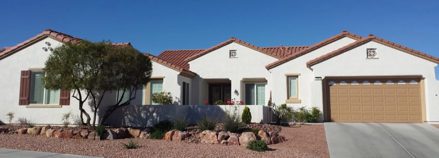 Finished white stucco home with a terracotta tile roof and tan garage door under a clear blue sky