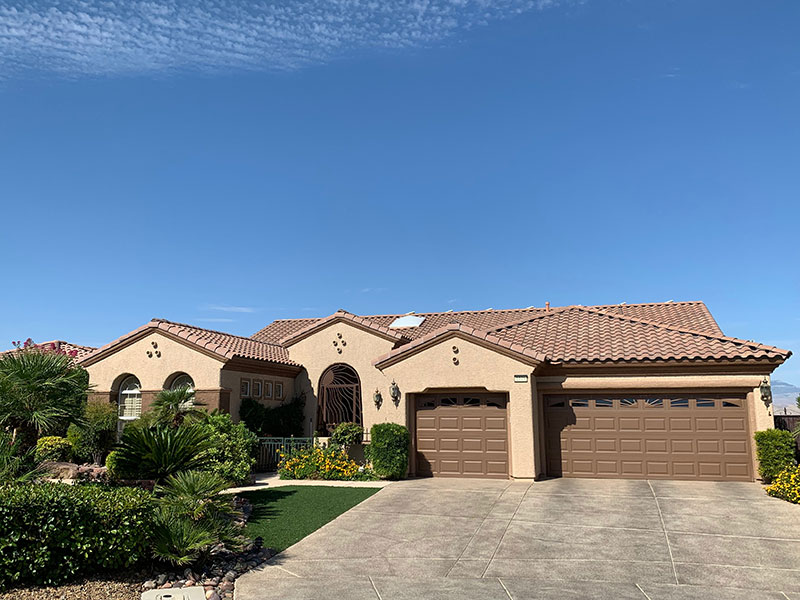 Finished tan home with two brown garage doors, an iron entry gate and a tile roof