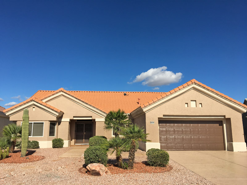 Finished tan home with a brown garage door, palms and an orange tile roof