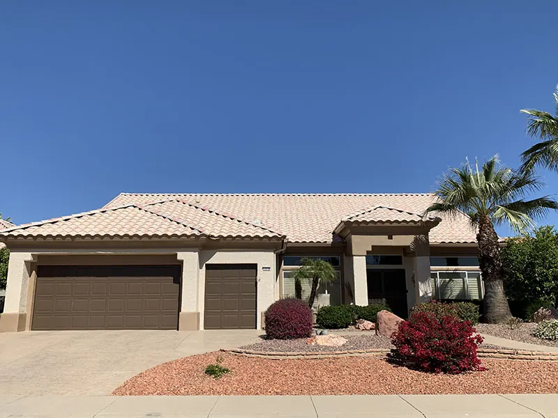 Finished beige home with a brown three-car garage and red shrubs