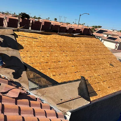 Roof sheathing exposed for inspection and repair beside stacked clay tiles