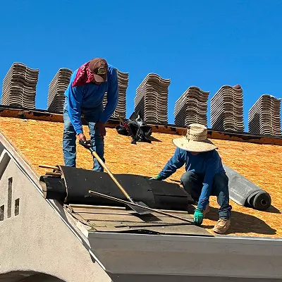 Two roofers removing and laying underlayment on an open tile roof
