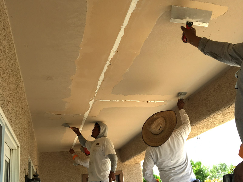Three McMillan painters scraping failed texture off a stucco patio ceiling