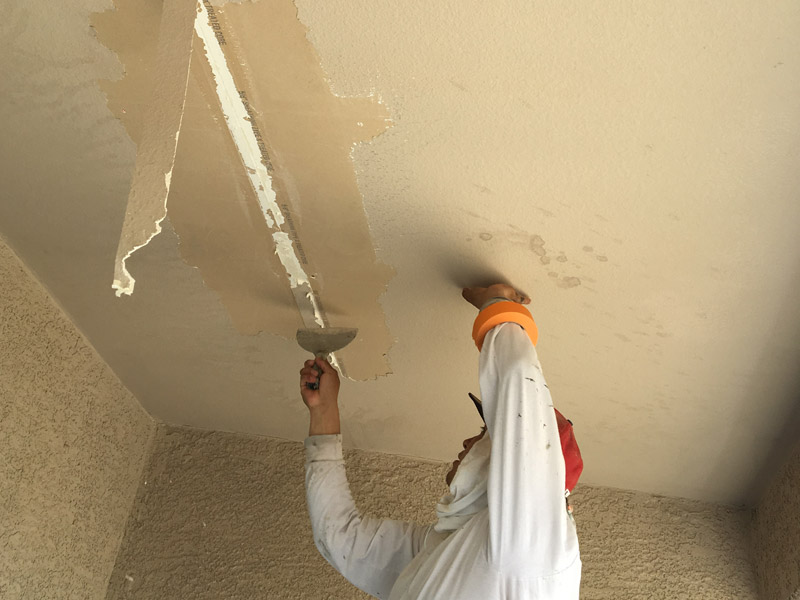 Painter in whites working a taped crack on a patio ceiling with a putty knife